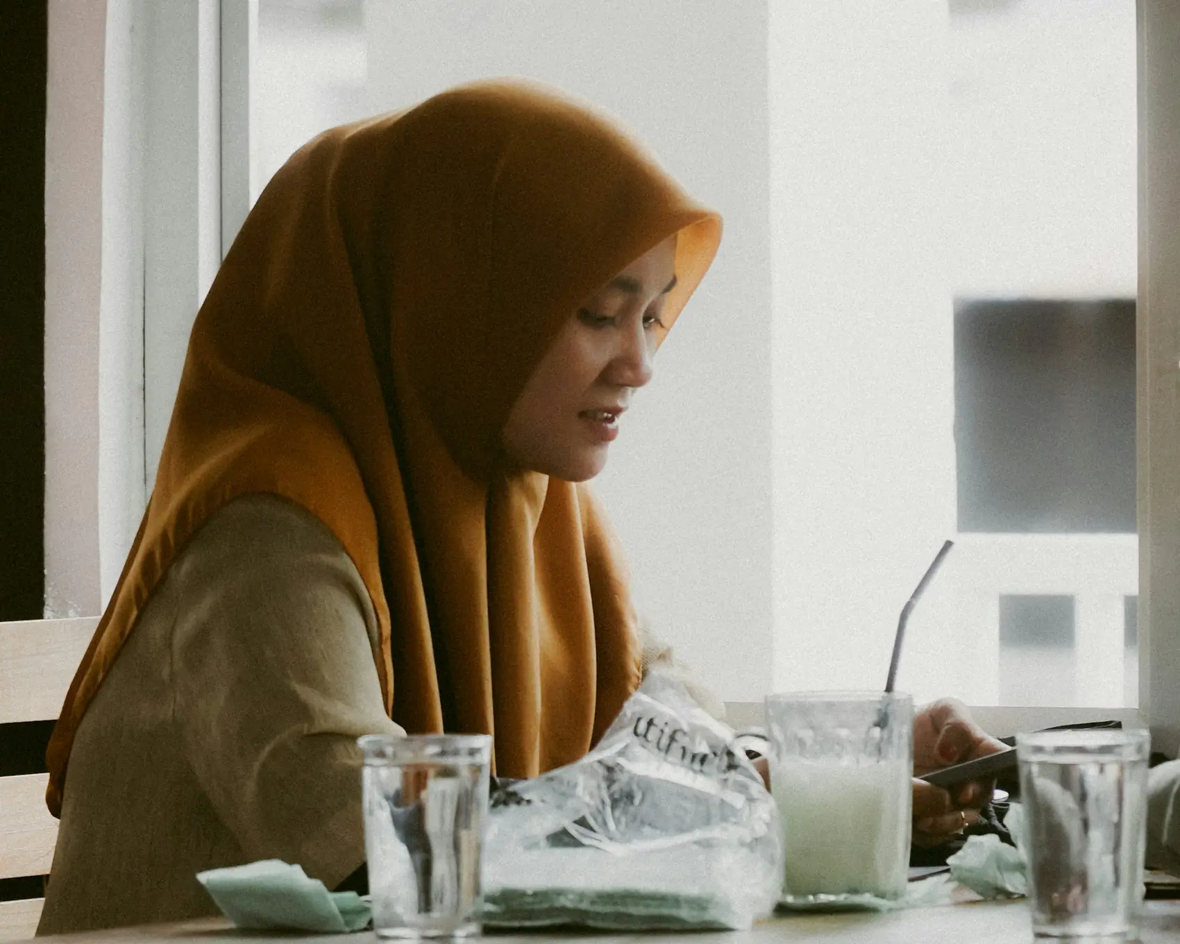A woman in a hijab working on her laptop in a café
